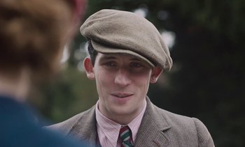 Movie still from “Mothering Sunday” (2021), directed by Eva Husson – A young man wearing a hat and a suit; Close Up shot, Over the shoulder angle
