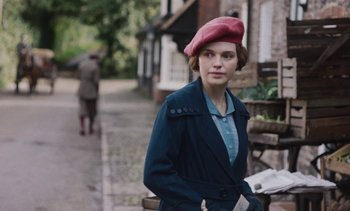 Movie still from “Mothering Sunday” (2021), directed by Eva Husson – A woman in a red hat and a blue jacket; Medium shot, Over the shoulder angle