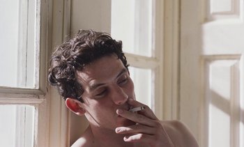 Movie still from “Mothering Sunday” (2021), directed by Eva Husson – A man smoking a cigarette in front of a window; Close Up shot, Low angle