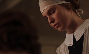 Movie still from “Mothering Sunday” (2021), directed by Eva Husson – A woman wearing a white hat looking down at her face; Close Up shot, Low angle