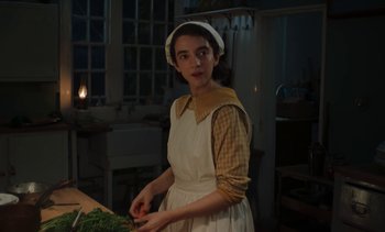 Movie still from “Mothering Sunday” (2021), directed by Eva Husson – A woman standing in front of a table with a bunch of food; Medium shot, Low angle