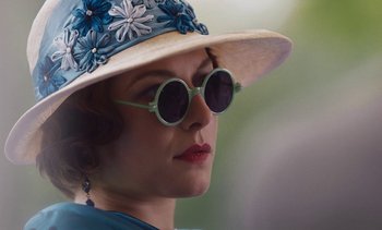 Movie still from “Mothering Sunday” (2021), directed by Eva Husson – A person wearing sunglasses and a hat; Close Up shot, Over the shoulder angle
