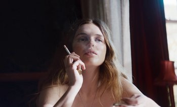 Movie still from “Mothering Sunday” (2021), directed by Eva Husson – A woman smoking a cigarette while sitting at a table; Close Up shot, High angle