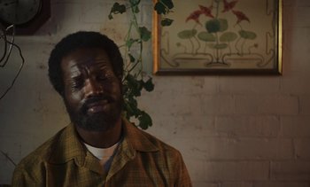 Movie still from “Mothering Sunday” (2021), directed by Eva Husson – A man in a brown shirt and a plant in the background; Close Up shot, Low angle