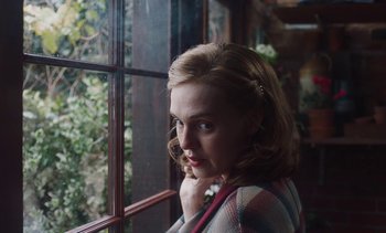 Movie still from “Mothering Sunday” (2021), directed by Eva Husson – A young woman is standing in front of a window; Close Up shot, Over the shoulder angle