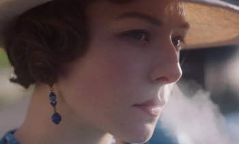 Movie still from “Mothering Sunday” (2021), directed by Eva Husson – A person wearing a hat and earrings; Extreme Close Up shot, Low angle