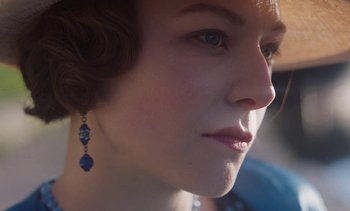 Movie still from “Mothering Sunday” (2021), directed by Eva Husson – A person wearing a necklace and earrings; Extreme Close Up shot, Over the shoulder angle