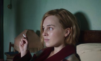 Movie still from “Mothering Sunday” (2021), directed by Eva Husson – A woman sitting in a chair holding a cigarette in her mouth; Close Up shot, High angle