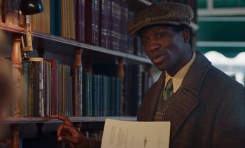 Movie still from “Mothering Sunday” (2021), directed by Eva Husson – A man is standing in front of a book shelf; Medium shot, Low angle