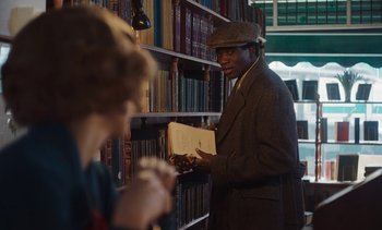 Movie still from “Mothering Sunday” (2021), directed by Eva Husson – A man holding a book in front of a woman; Medium shot, Over the shoulder angle