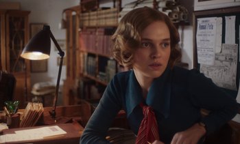 Movie still from “Mothering Sunday” (2021), directed by Eva Husson – A woman sitting at a table in a room; Medium shot, Over the shoulder angle