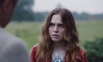 Movie still from “Mothering Sunday” (2021), directed by Eva Husson – A woman with long brown hair and blue eyes stares into the camera; Close Up shot, Over the shoulder angle