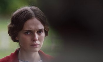 Movie still from “Mothering Sunday” (2021), directed by Eva Husson – A young woman with brown hair wearing a red jacket; Close Up shot, Over the shoulder angle