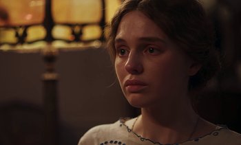 Movie still from “Mothering Sunday” (2021), directed by Eva Husson – A young woman looking into the distance in a dark room; Close Up shot, Over the shoulder angle
