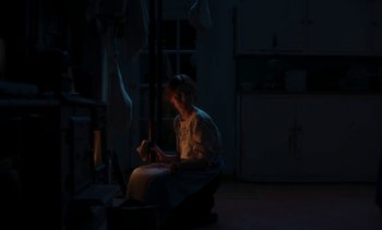 Movie still from “Mothering Sunday” (2021), directed by Eva Husson – A person sitting in a dark room reading a book; Medium shot, Low angle