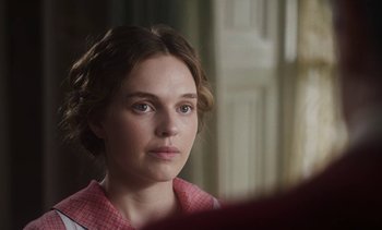 Movie still from “Mothering Sunday” (2021), directed by Eva Husson – A young woman looking into a mirror while wearing a red checkered shirt; Close Up shot, Over the shoulder angle