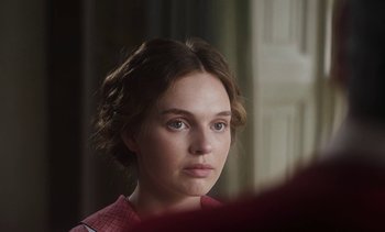 Movie still from “Mothering Sunday” (2021), directed by Eva Husson – A young woman with blue eyes stares into the camera; Close Up shot, Over the shoulder angle