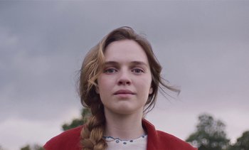 Movie still from “Mothering Sunday” (2021), directed by Eva Husson – A young woman with a braid and a red jacket; Close Up shot, Low angle