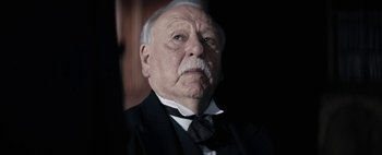 Movie still from “Mr. Jones” (2019), directed by Agnieszka Holland – An older man in a black suit and a black tie; Close Up shot, Low angle