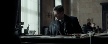 Movie still from “Mr. Jones” (2019), directed by Agnieszka Holland – A man sitting at a table with a cup of coffee in front of him; Medium shot, Low angle