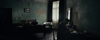 Movie still from “Mr. Jones” (2019), directed by Agnieszka Holland – A man sitting at a table in a living room next to a window; Wide shot, Low angle