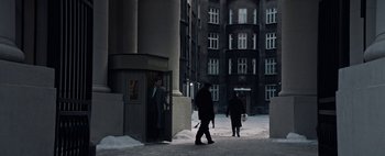Movie still from “Mr. Jones” (2019), directed by Agnieszka Holland – Two people walking on a snowy sidewalk in front of a tall building; Extreme Wide shot, High angle