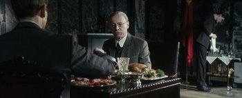 Movie still from “Mr. Jones” (2019), directed by Agnieszka Holland – An older man sitting at a table with a plate of food; Medium shot, Over the shoulder angle