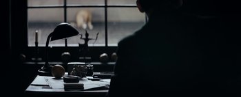 Movie still from “Mr. Jones” (2019), directed by Agnieszka Holland – A person sitting at a table with a cat in the background; Medium shot, Over the shoulder angle