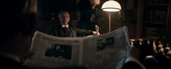 Movie still from “Mr. Jones” (2019), directed by Agnieszka Holland – A man sitting in front of a newspaper in a room; Medium shot, Over the shoulder angle