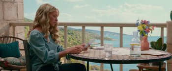 Movie still from “Mamma Mia! Here We Go Again” (2018), directed by Ol Parker – A woman sitting at an outdoor table looking at her cell phone; Medium shot, High angle