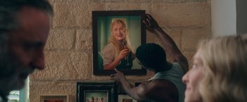Movie still from “Mamma Mia! Here We Go Again” (2018), directed by Ol Parker – A man hanging a picture of a woman on the wall; Close Up shot, Over the shoulder angle