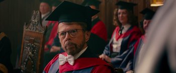 Movie still from “Mamma Mia! Here We Go Again” (2018), directed by Ol Parker – A man wearing a graduation cap and gown; Close Up shot, Over the shoulder angle