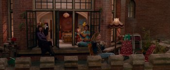 Movie still from “Mamma Mia! Here We Go Again” (2018), directed by Ol Parker – Two women sitting on steps in front of a brick building; Wide shot, High angle