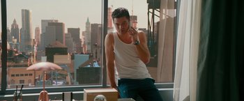 Movie still from “Mamma Mia! Here We Go Again” (2018), directed by Ol Parker – A man in a tank top talking on a cell phone in front of a window; Medium shot, Over the shoulder angle