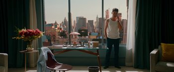 Movie still from “Mamma Mia! Here We Go Again” (2018), directed by Ol Parker – A man standing in front of a large window with a view of a city; Wide shot, High angle