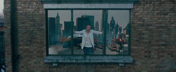 Movie still from “Mamma Mia! Here We Go Again” (2018), directed by Ol Parker – A man standing in front of a large window with his arms outstretched; Wide shot, Overhead angle