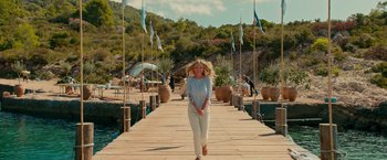 Movie still from “Mamma Mia! Here We Go Again” (2018), directed by Ol Parker – A woman is walking on a pier near a body of water; Extreme Wide shot, Over the shoulder angle
