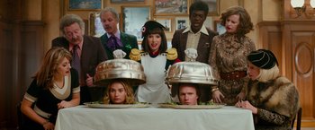 Movie still from “Mamma Mia! Here We Go Again” (2018), directed by Ol Parker – A group of people standing around a table with plates of food on top of it; Medium shot, Over the shoulder angle