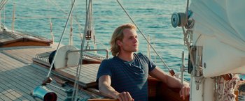 Movie still from “Mamma Mia! Here We Go Again” (2018), directed by Ol Parker – A man sitting on a sailboat in the water; Medium shot, Low angle