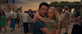 Movie still from “Mamma Mia! Here We Go Again” (2018), directed by Ol Parker – A man and a woman hugging each other in front of a crowd of onlookers; Medium shot, Overhead angle