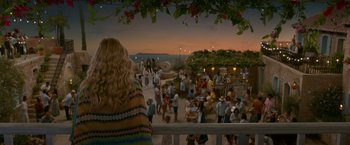 Movie still from “Mamma Mia! Here We Go Again” (2018), directed by Ol Parker – A crowd of people gathered on a pier at sunset; Wide shot, Over the shoulder angle
