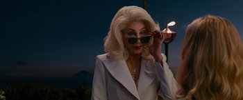 Movie still from “Mamma Mia! Here We Go Again” (2018), directed by Ol Parker – An older woman in a white suit and sunglasses; Medium shot, Over the shoulder angle