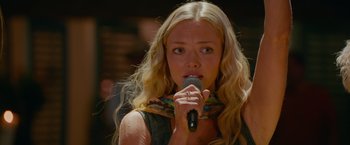 Movie still from “Mamma Mia! Here We Go Again” (2018), directed by Ol Parker – A beautiful blonde woman holding a microphone up to her mouth; Close Up shot, Over the shoulder angle