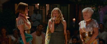 Movie still from “Mamma Mia! Here We Go Again” (2018), directed by Ol Parker – A woman standing in front of a crowd holding a microphone; Medium shot, Over the shoulder angle