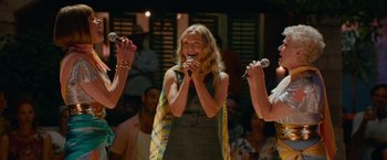 Movie still from “Mamma Mia! Here We Go Again” (2018), directed by Ol Parker – A group of people singing into microphones in front of an audience; Medium shot, Low angle