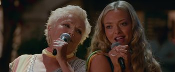 Movie still from “Mamma Mia! Here We Go Again” (2018), directed by Ol Parker – Two women sing into microphones in front of each other; Close Up shot, Low angle