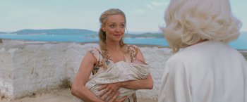 Movie still from “Mamma Mia! Here We Go Again” (2018), directed by Ol Parker – A woman holding a baby in her arms and smiling; Close Up shot, Over the shoulder angle