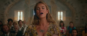 Movie still from “Mamma Mia! Here We Go Again” (2018), directed by Ol Parker – A woman with long blonde wavy hair wearing a butterfly necklace; Close Up shot, Low angle