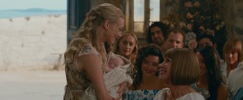 Movie still from “Mamma Mia! Here We Go Again” (2018), directed by Ol Parker – A group of people standing around a baby; Close Up shot, Over the shoulder angle