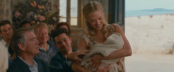 Movie still from “Mamma Mia! Here We Go Again” (2018), directed by Ol Parker – A man and woman holding a baby in a room; Medium shot, Over the shoulder angle